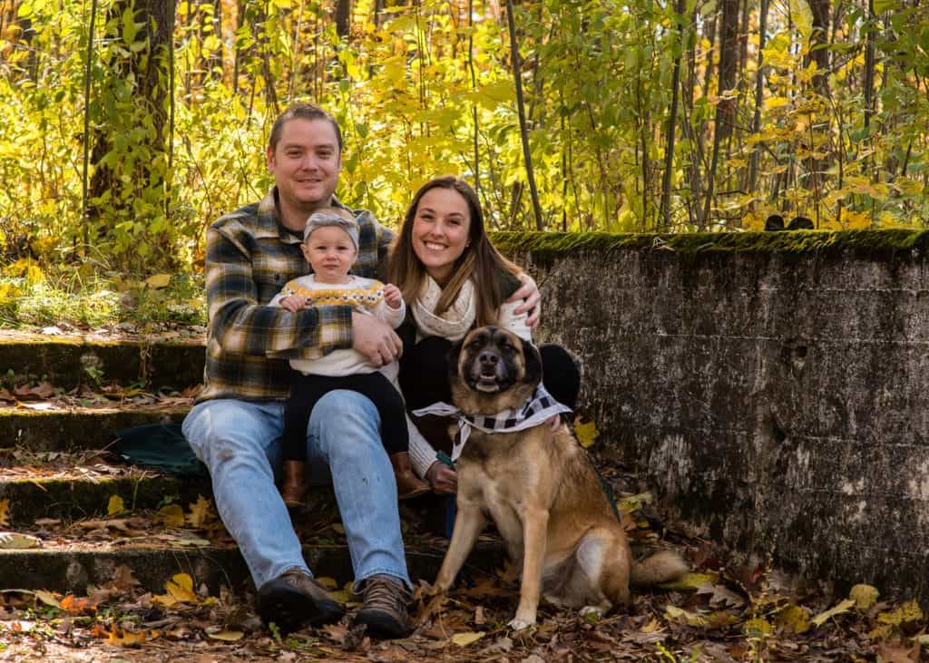 Three people  and a dog sitting on a bench posing for the camera