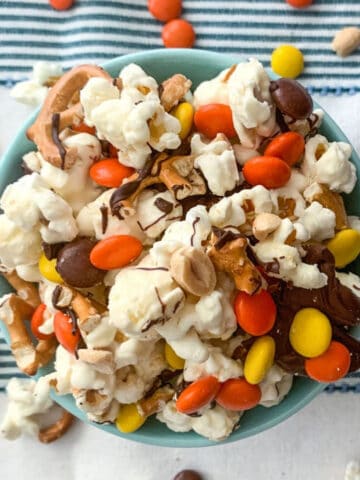 A bowl of popcorn topped with chocolate, pretzels, and candy.