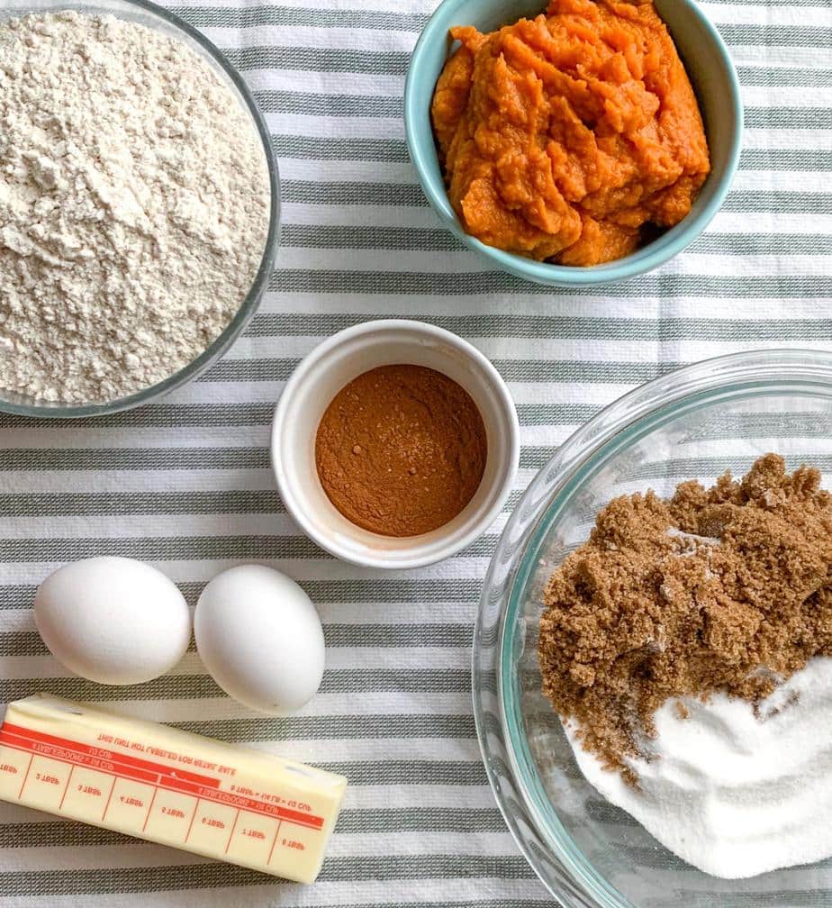 Top down view of Ingredients for the pumpkin bread- canned pumpkin, spices, flour, brown and white sugar, eggs, and butter.