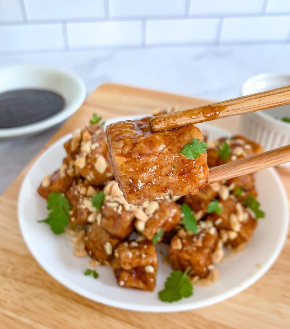 A close up of fried tofu between two chopsticks. 