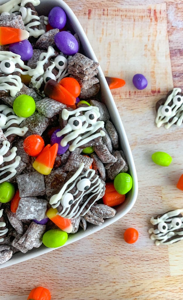 A bowl of chocolate covered chex, topped with decorated pretzels and colored M&Ms.