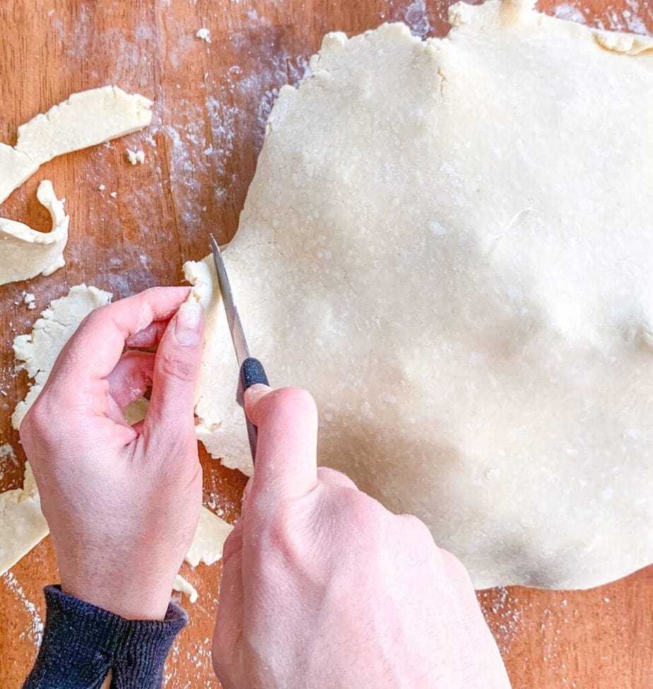 Two hands trimming pie crust with a small knife.