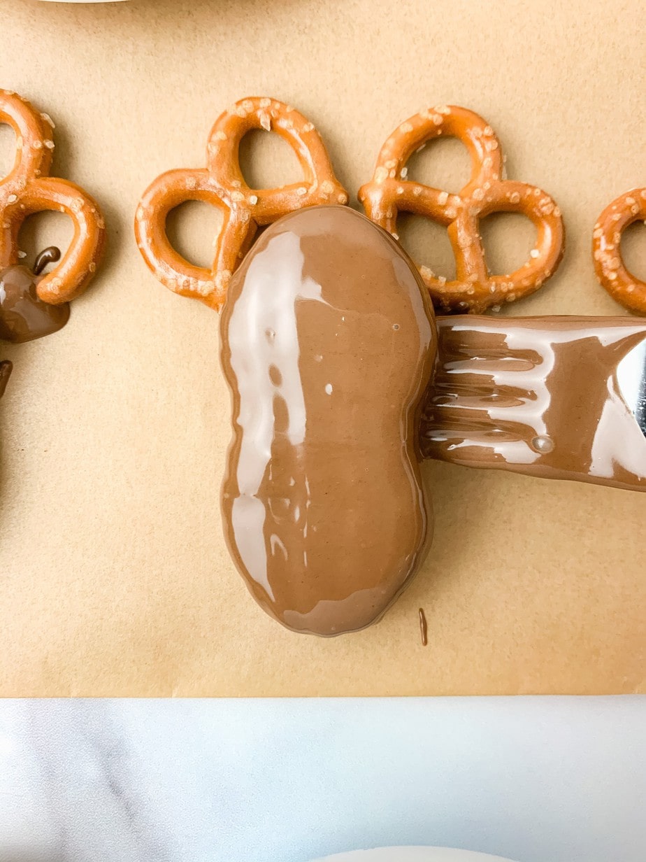 A chocolate dipped Nutter Butter being placed on two pretzels with a fork, on brown parchment paper.