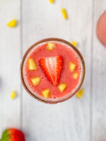 Overhead photo of a strawberry smoothie in a glass. A garnish of diced pineapple and sliced strawberry on top.