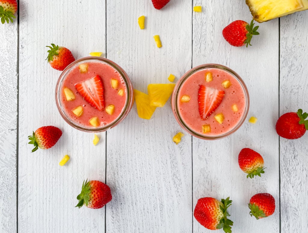 Two top down images of smoothies with fresh strawberries and pineapple on top and around the glasses.