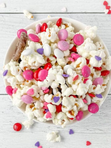 A bowl of popcorn topped with pink and purple candies