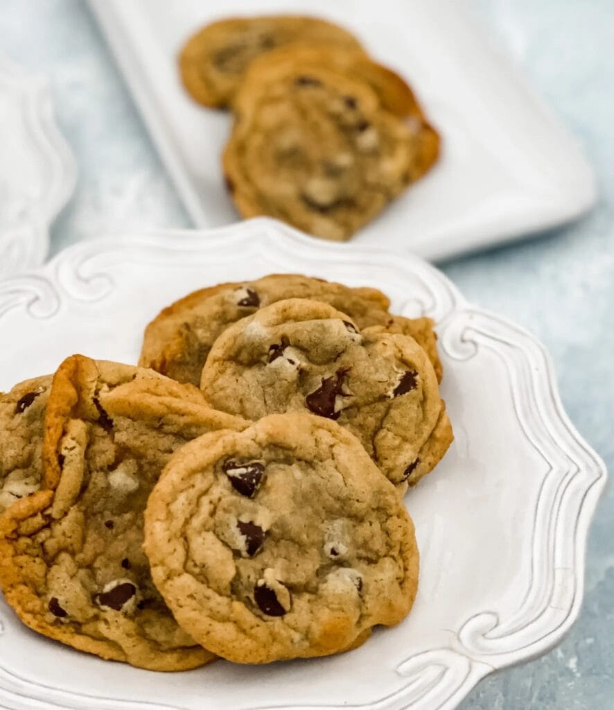 Piled chocolate chip cookies on a white plate.