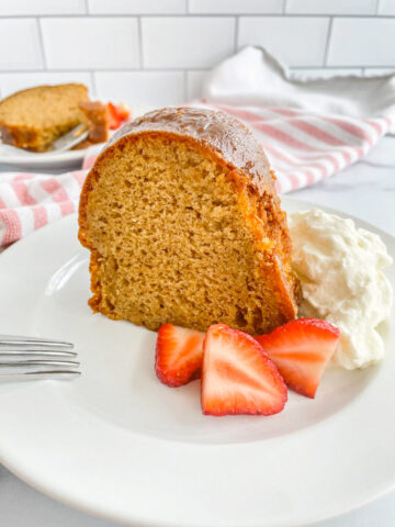 A slices of bundt cake on a white plate, garnished with whipped cream and strawberries.