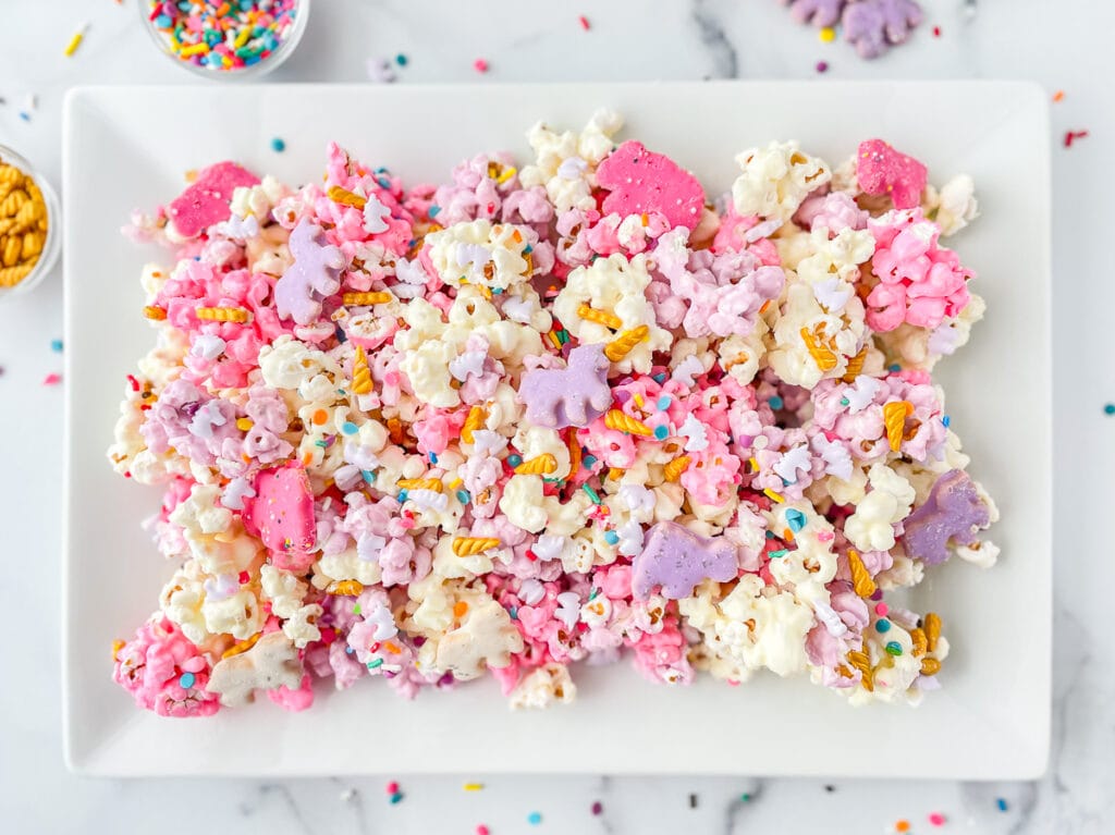 A platter full of pink, white, purple candy coated popcorn, decorated with sprinkles.