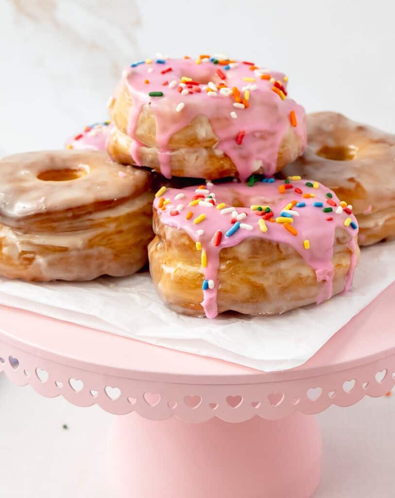 A doughnut sitting on top of a cake stand, with pink glaze and sprinkles.