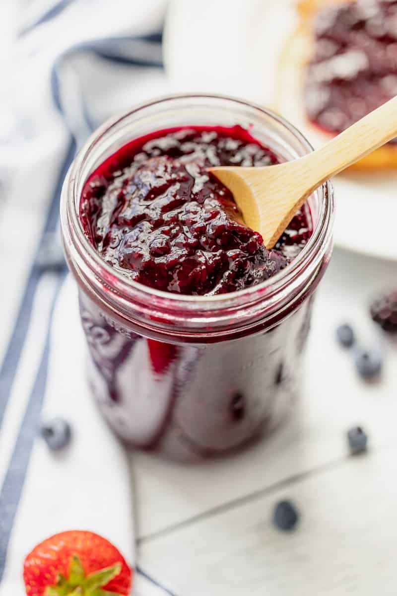 A jar of mixed berry jam with toast and fresh berries