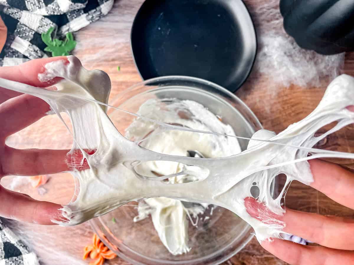 Fingers spread apart with melted marshmallows spread between the fingers, making a spider web