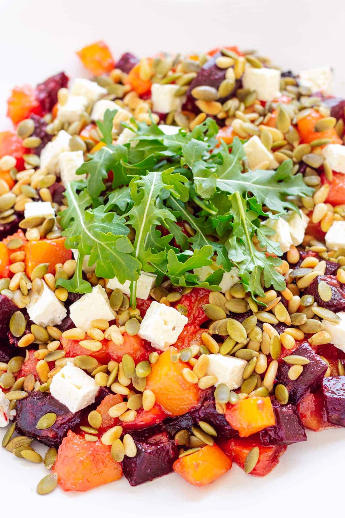 A pile of cubed beets, pumpkin, feta, pumpkin seeds and pine nuts, topped with arugula.