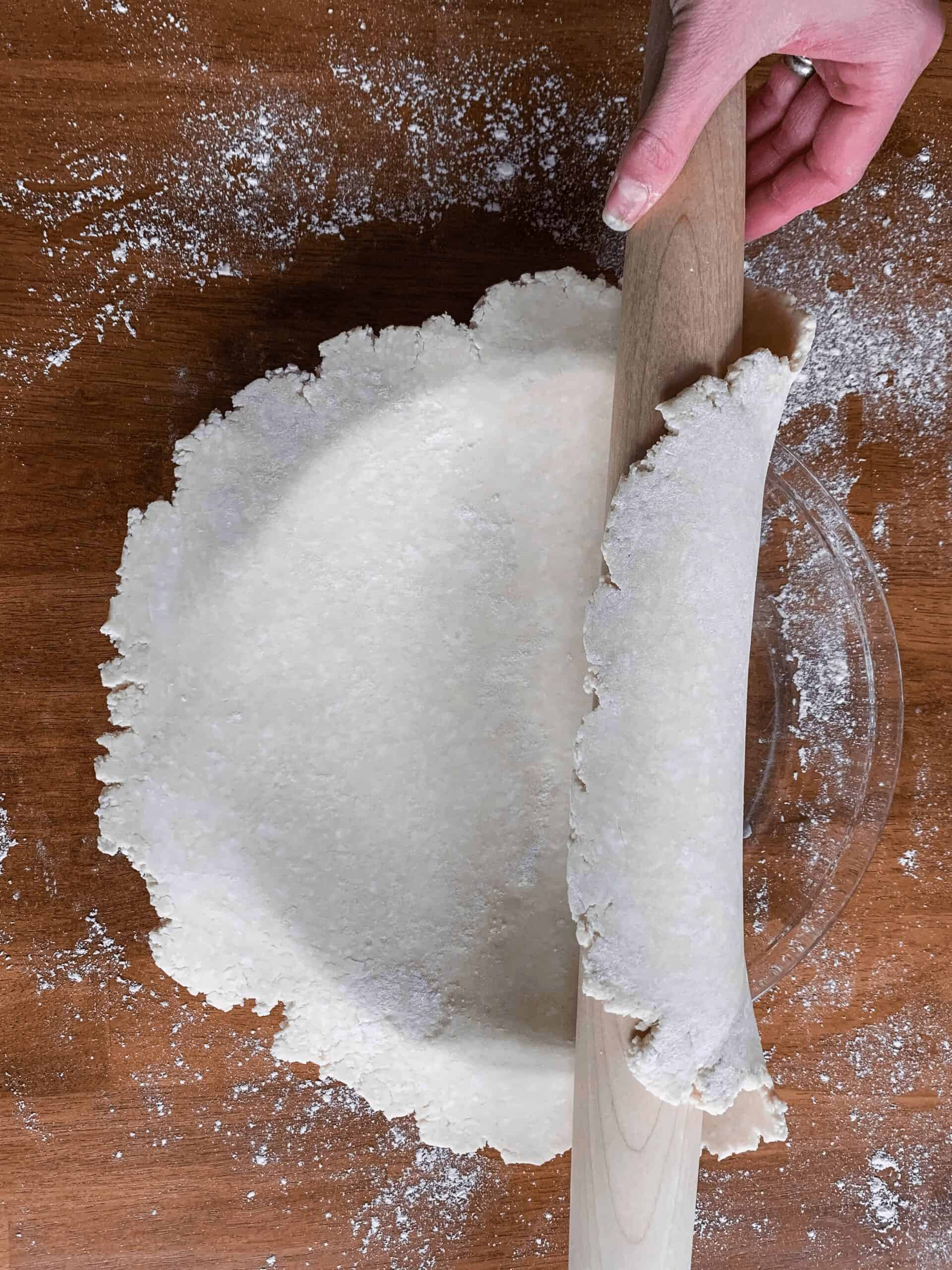 Using a rolling pin to lay the pie dough across the pie plate.