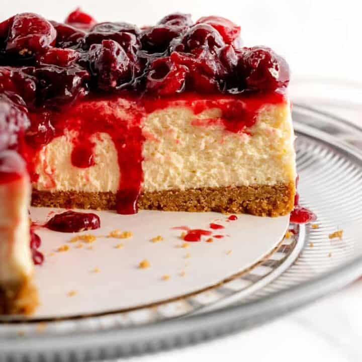 A cheesecake with cherry topping, a slice missing and cherry juice dripping inside.