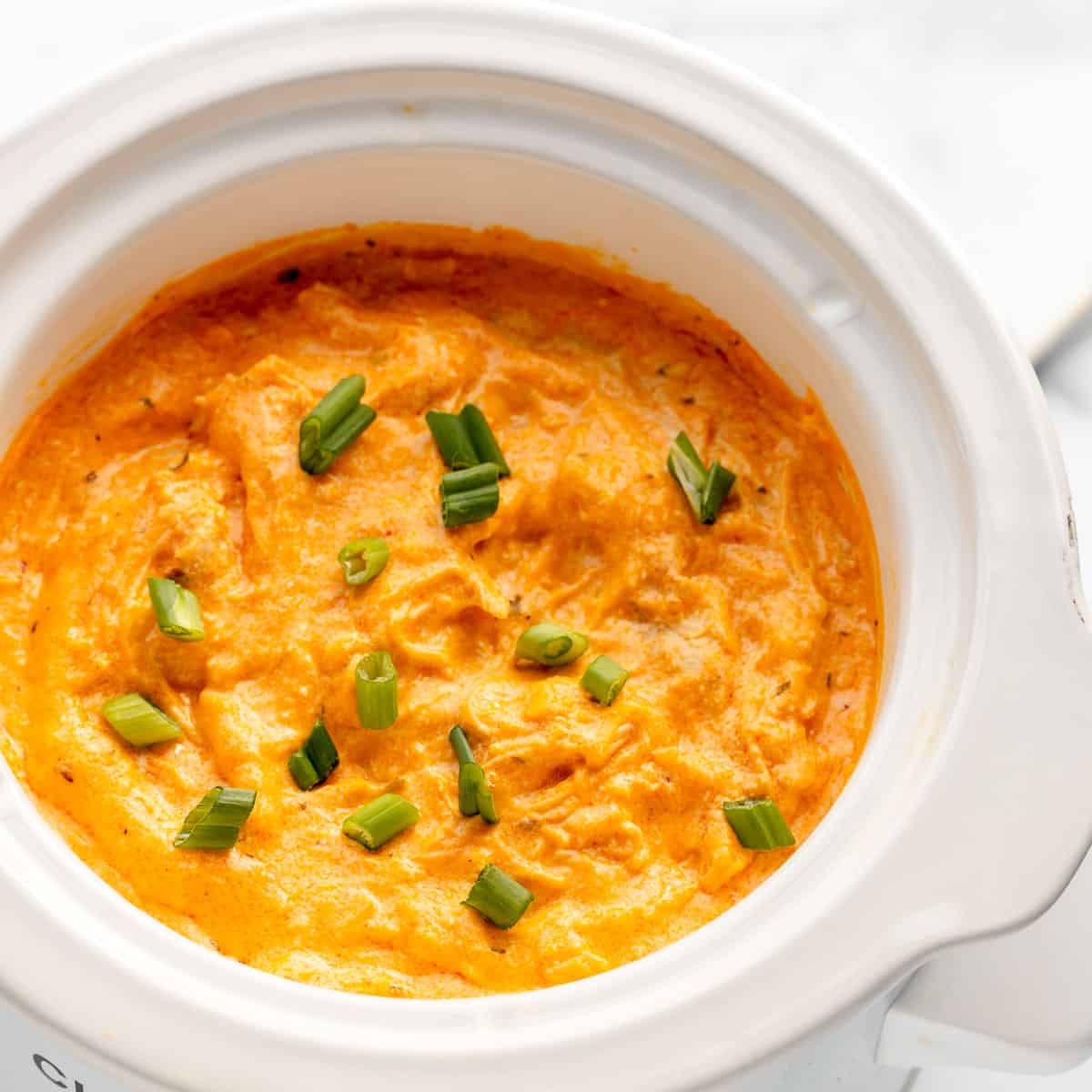 Finished buffalo chicken dip topped with scallions in a white slow cooker