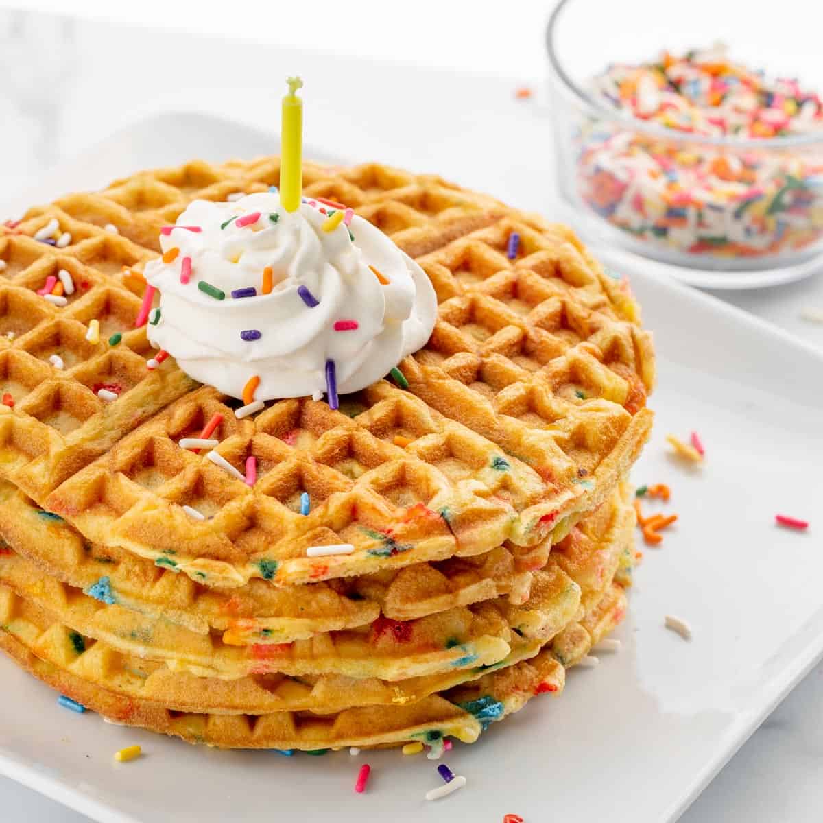 Photo of a stack of waffles with whipped cream, birthday candle and sprinkles.