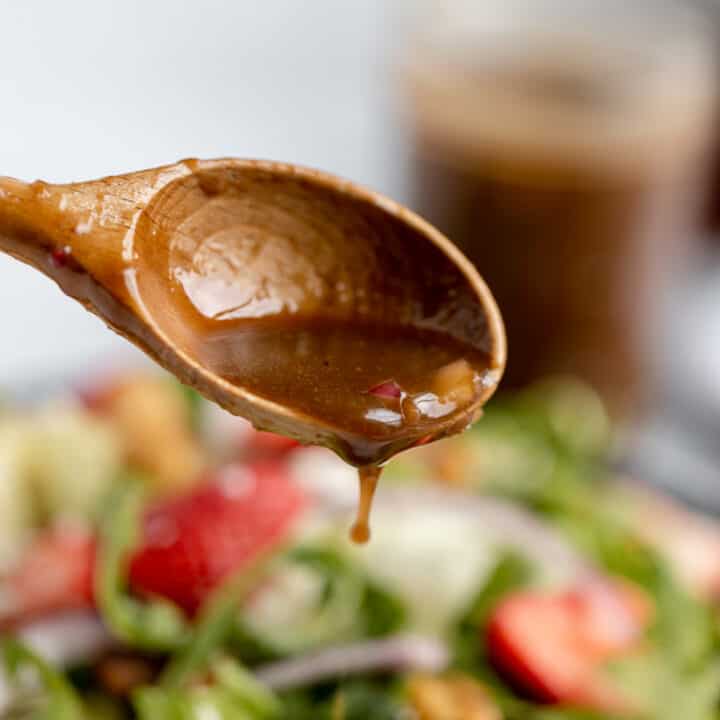 A wooden spoon with balsamic dressing running off.