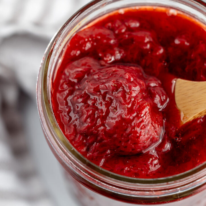 A wooden spoon scooping strawberry compote out of a jar