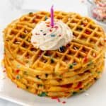 Stack of waffles topped with sprinkles, whipped cream and a candle.
