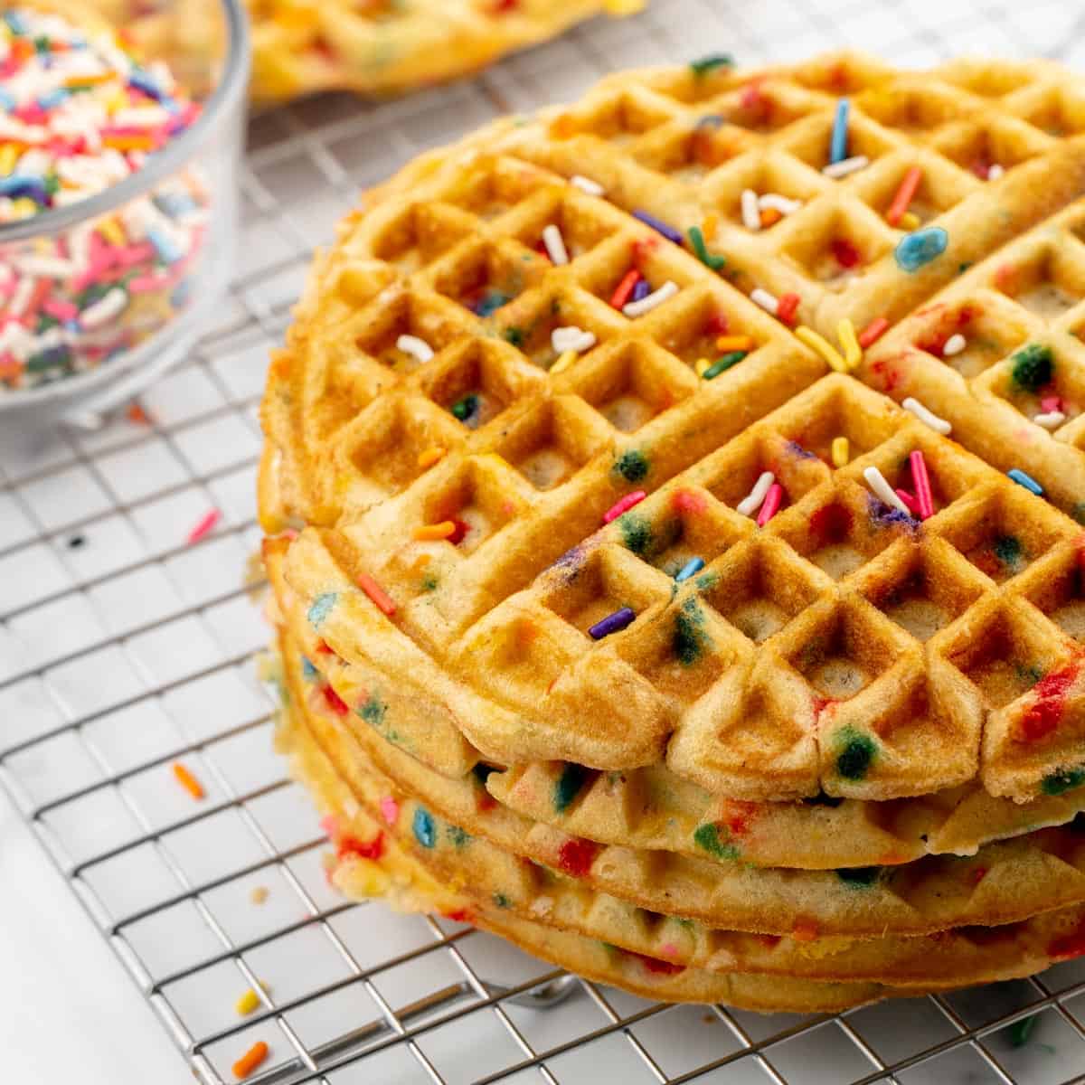 A stack of birthday cake waffles on a wire rack with sprinkles.