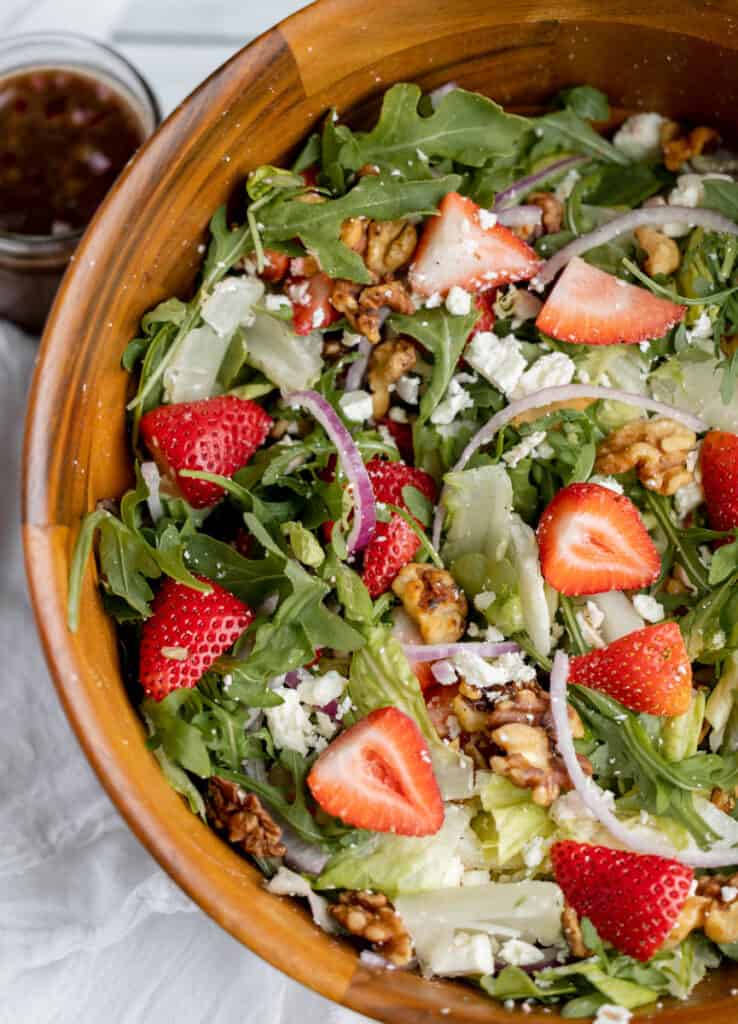 Strawberry and walnut salad with leafy greens and feta in a wooden bowl.