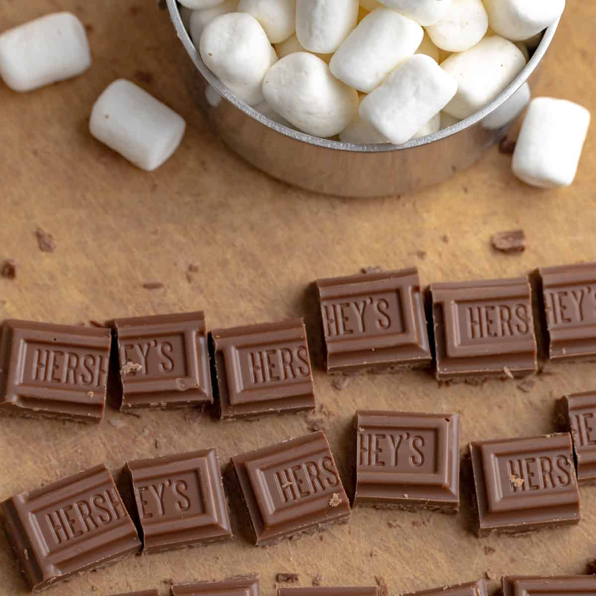 cut up chocolate candy bars on a cutting board. Marshmallows in the background