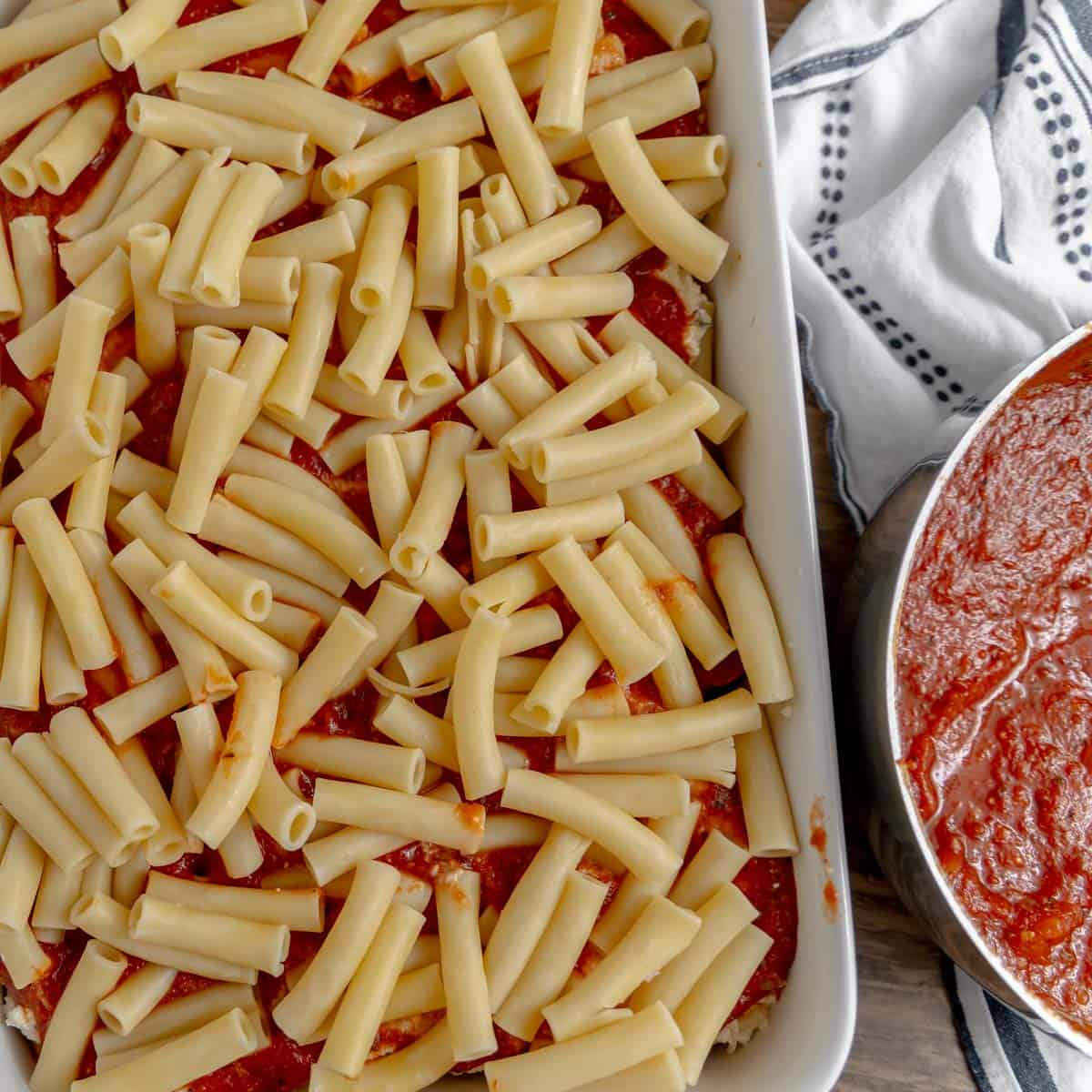 Ziti on top of sauce in a pan. Extra sauce on the side.