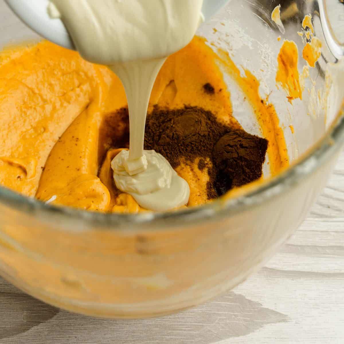 Pouring white chocolate in the bowl with pumpkin, cream cheese and spices.