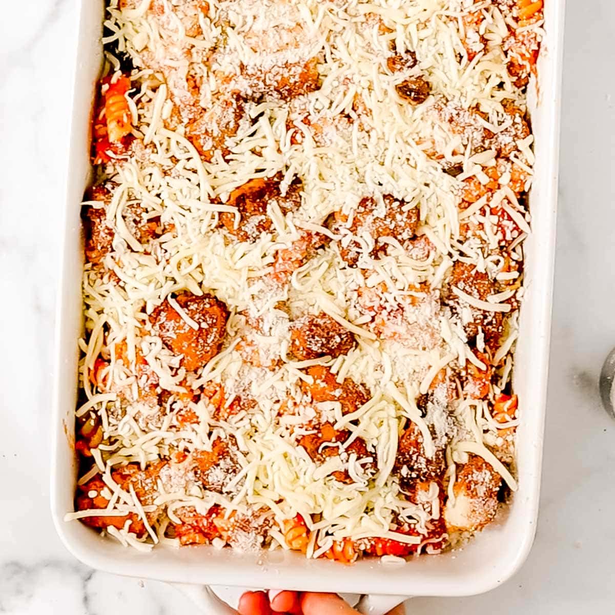 A casserole dish filled with pasta, meatballs, marinara sauce, and topped with shredded mozzarella and grated parmesan cheese.