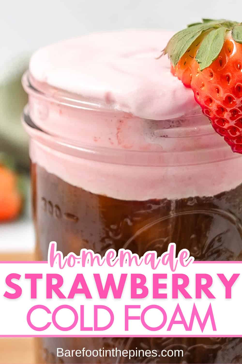 A glass jar filled with iced coffee topped with a thick layer of Strawberry Cold Foam, garnished with a fresh strawberry. Text reads "homemade strawberry cold foam.