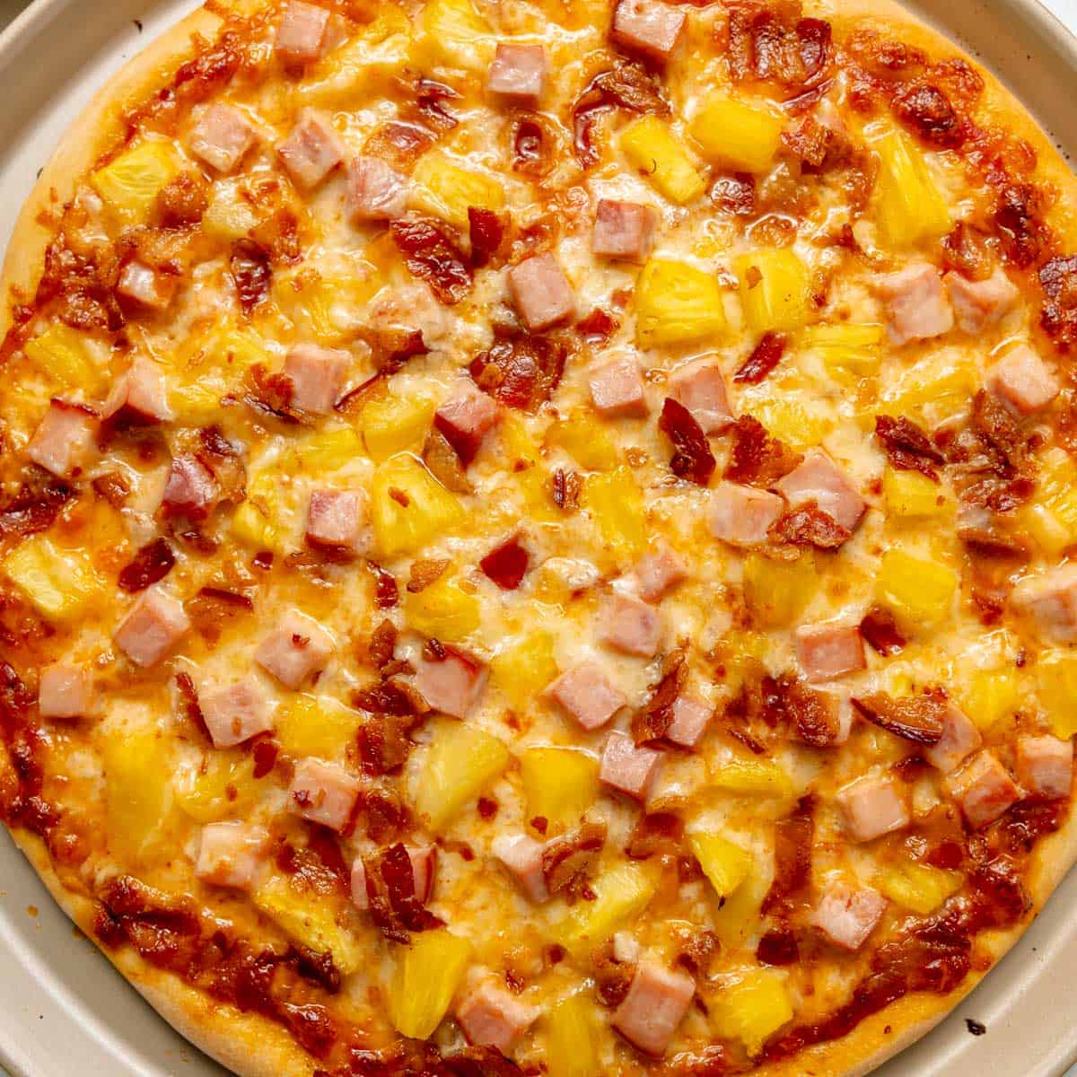 A Hawaiian pizza topped with diced ham, pineapple chunks, bacon pieces, and melted cheese on a round pizza crust.
