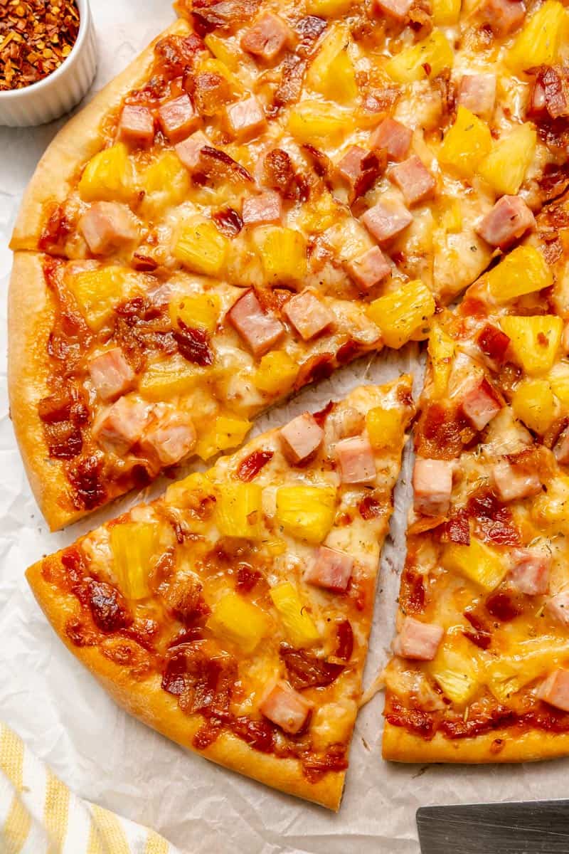 A Hawaiian pizza topped with ham, pineapple, and cheese, sliced with one piece slightly pulled out from the whole pizza.