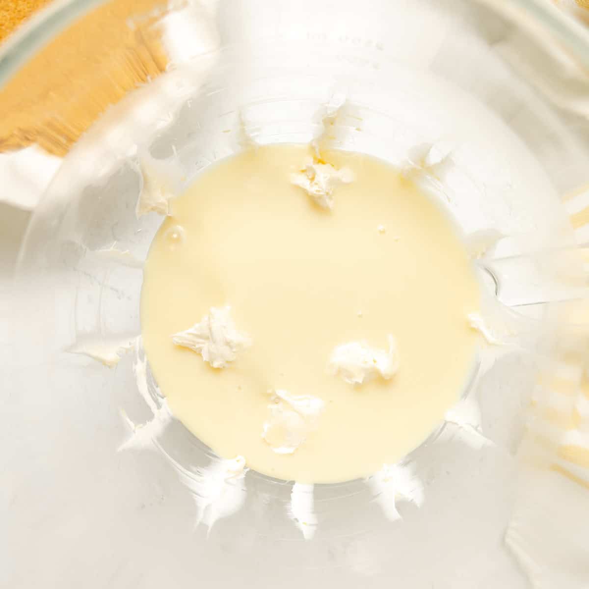 A glass mixing bowl containing a small amount of thick white cream and pale liquid, partially blended together.