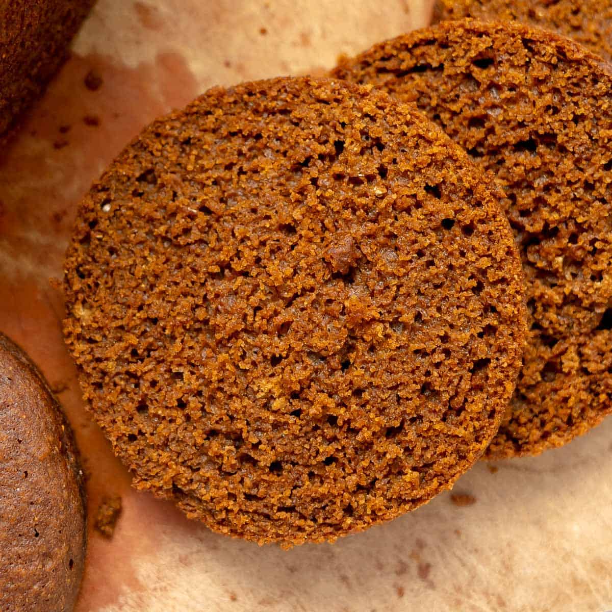 Two slices of dark brown bread lie on parchment paper, showing a moist and slightly crumbly texture.
