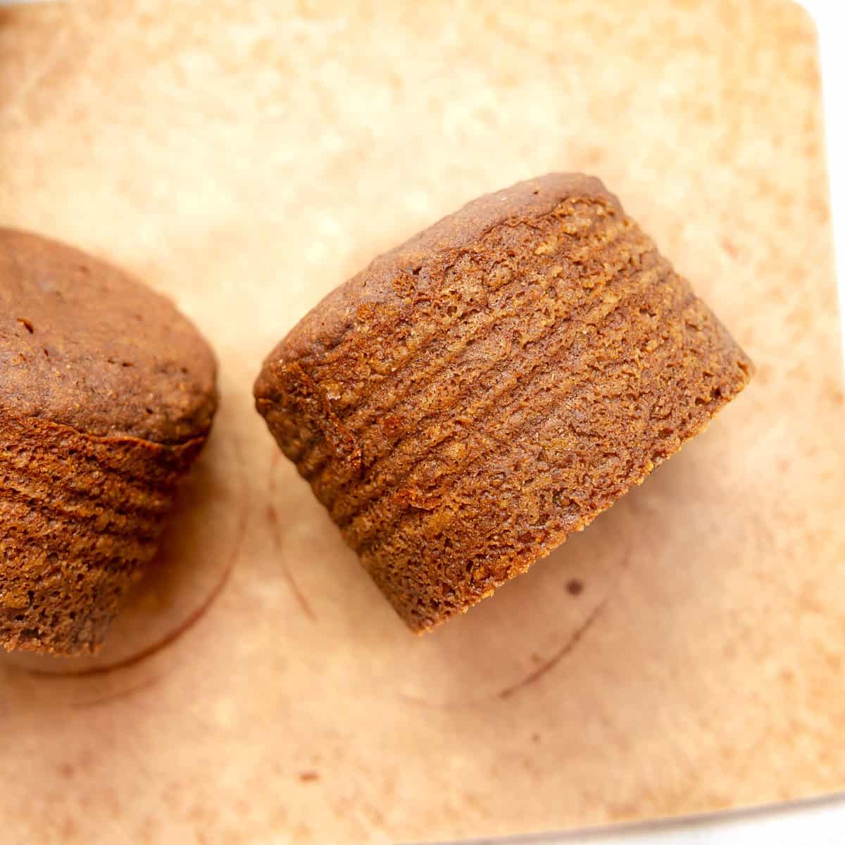 Two brown, round baked goods with textured sides, placed on a light brown surface.