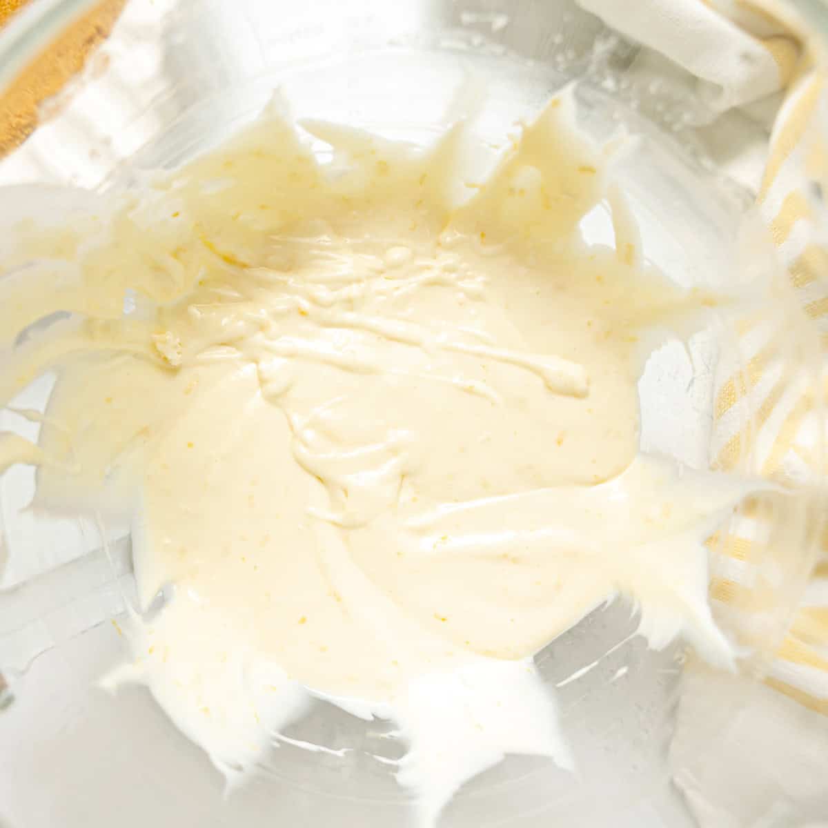 A glass bowl containing a small amount of creamy, pale yellow mixture, partially spread on the sides of the bowl.