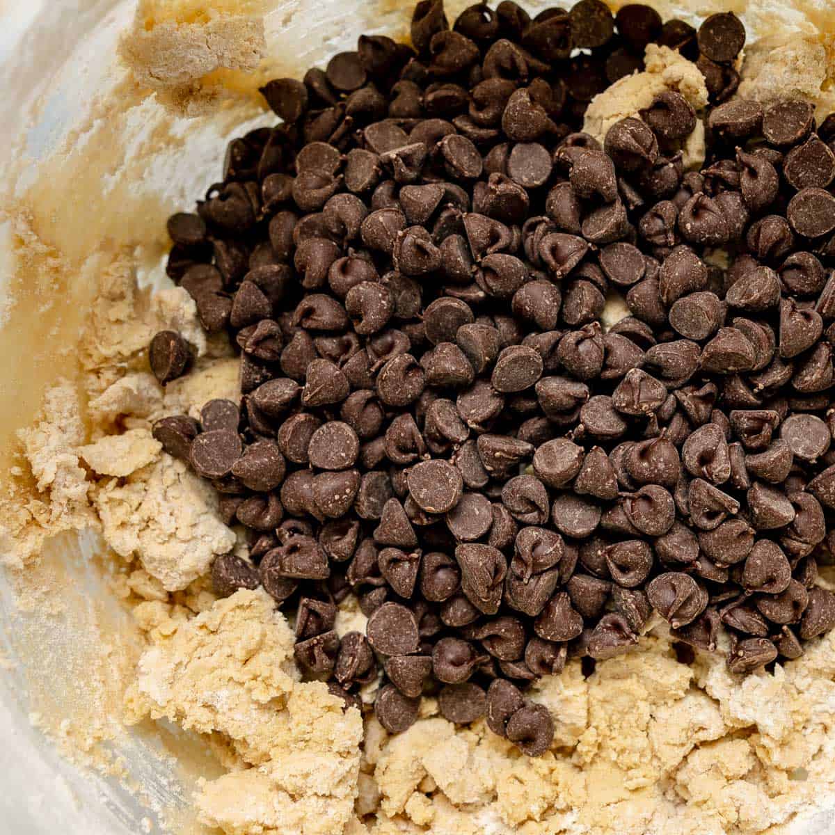 A pile of mini chocolate chips sits on top of raw cookie dough in a bowl.