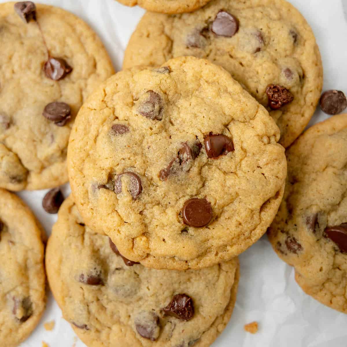 A close-up of several chocolate chip cookies stacked and overlapping on a white surface.