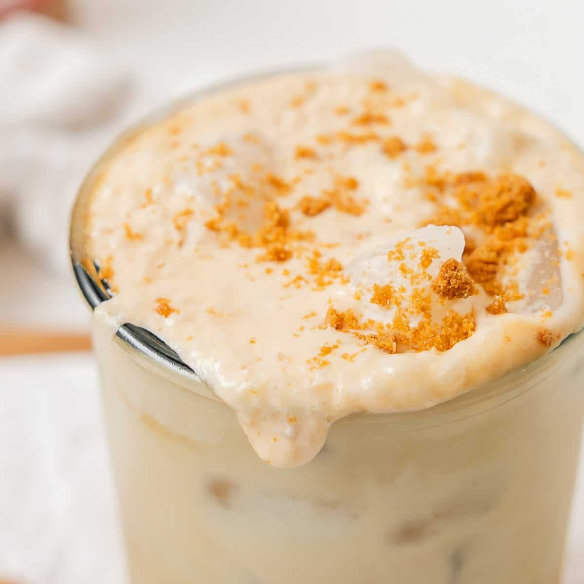 A close-up of a creamy iced beverage in a glass, topped with crushed cookie crumbs and ice, slightly overflowing at the rim.