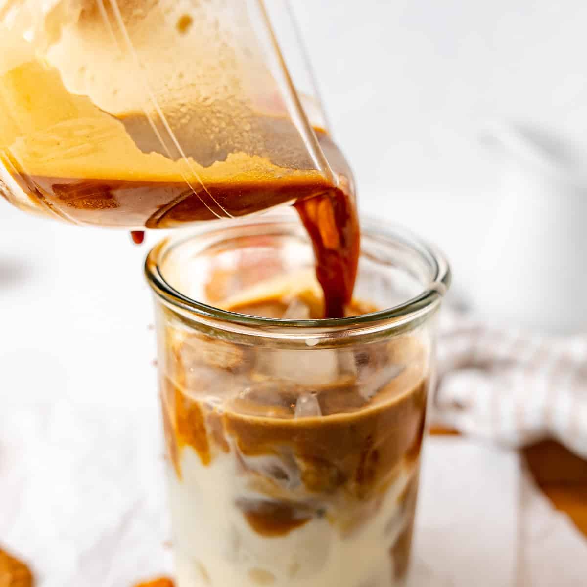 Espresso is being poured from a cup into a glass of iced milk, creating an iced coffee drink.