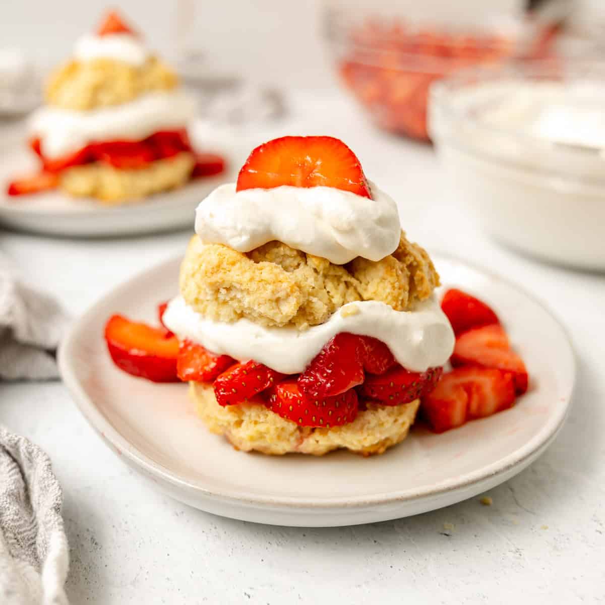A plate of strawberry shortcake with sliced strawberries and whipped cream between and on top of two biscuit halves.
