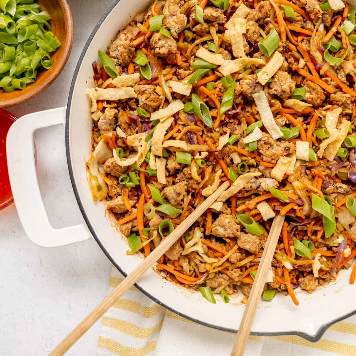 A skillet filled with a mixture of ground meat, shredded carrots, cabbage, green onions, and crispy wonton strips, with chopsticks resting on top.