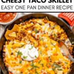 A cheesy Taco Skillet with melted cheese, beans, and vegetables in a cast iron pan, topped with fresh cilantro and served alongside tortilla chips and zesty salsa.