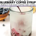 Hand stirring blueberry coffee syrup into a glass of iced coffee, with a bowl of blueberries in the background and text overlay about this easy blueberry coffee syrup recipe.