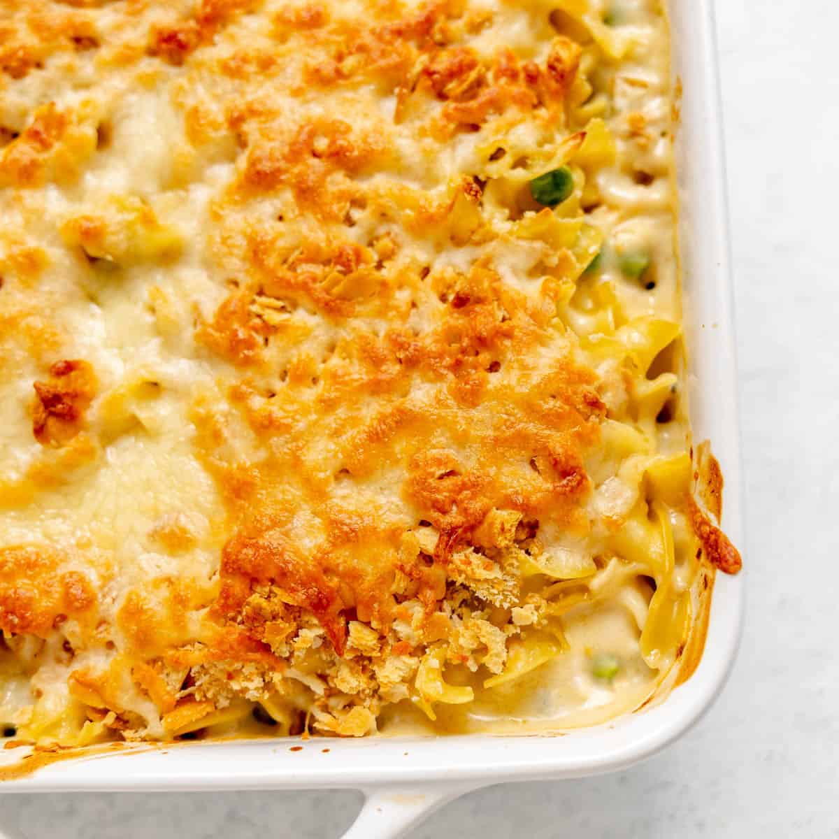 A baked casserole topped with melted, golden-brown cheese and crisp crumbs in a white dish, with pasta and vegetables visible underneath.