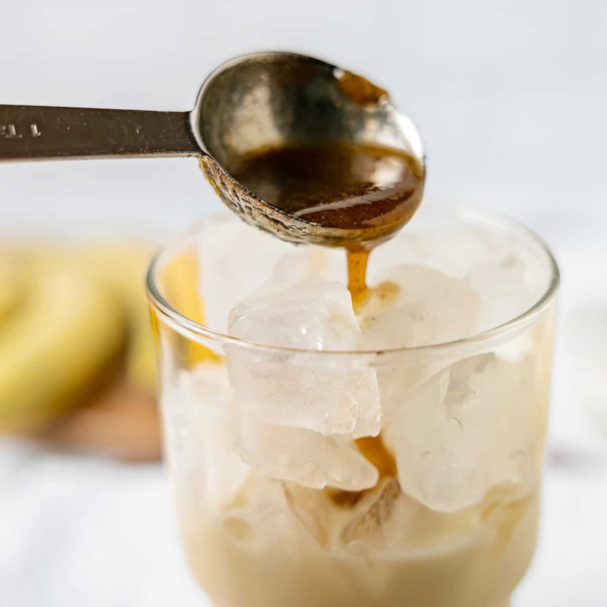 A spoon pours dark syrup over ice in a glass filled with milk.
