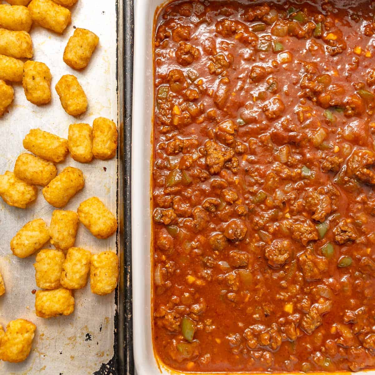 Rectangular baking pan with meat and tomato sauce next to a tray with scattered golden tater tots on a metal baking sheet.