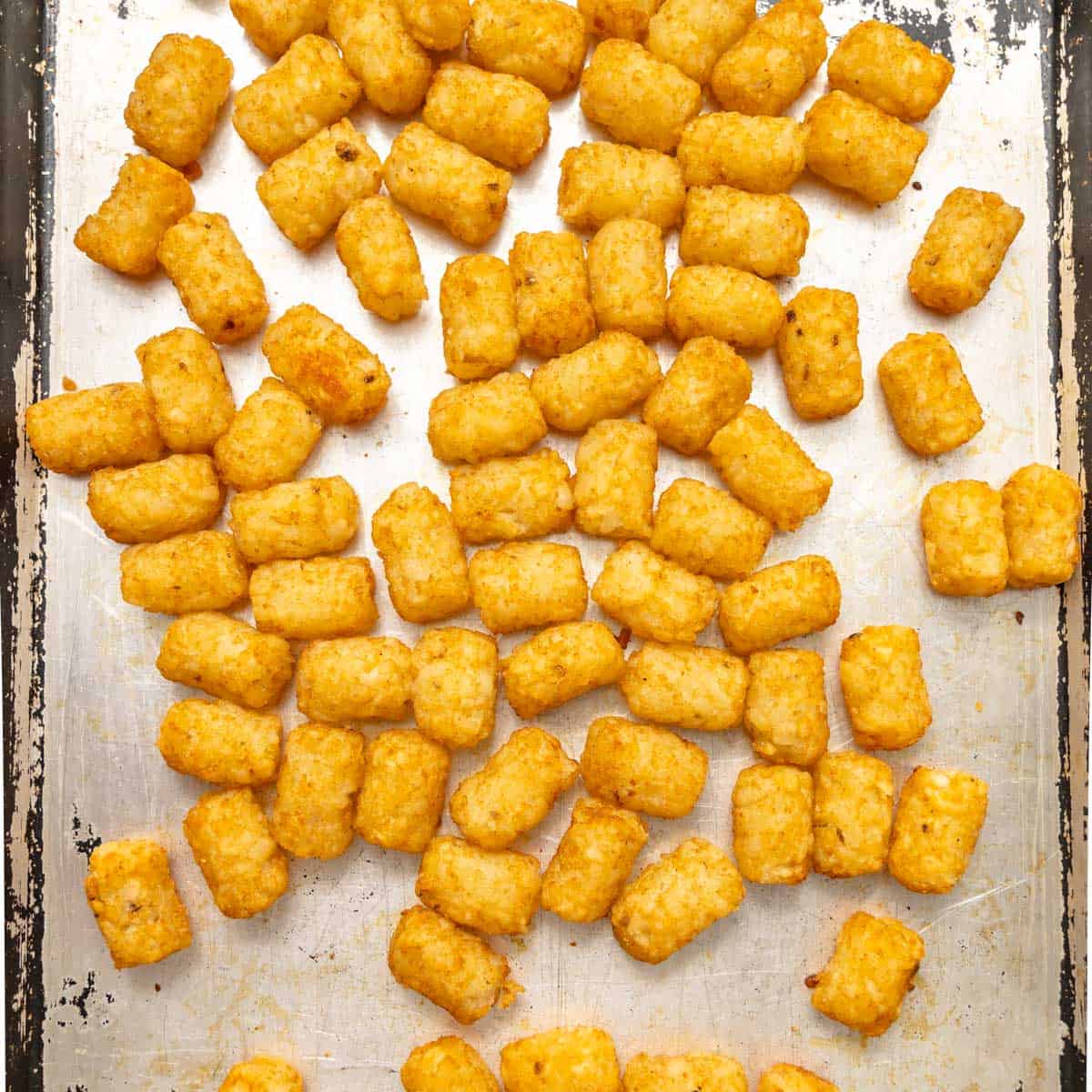 Golden tater tots scattered on a silver baking sheet, showing a crispy exterior and uneven arrangement.