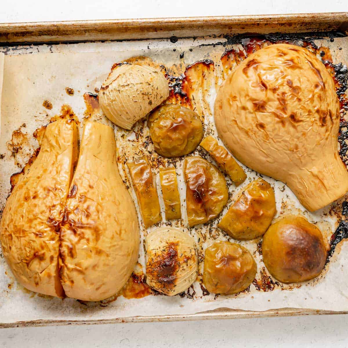 Roasted butternut squash halves and pieces on a parchment-lined baking sheet, cooked until golden brown.